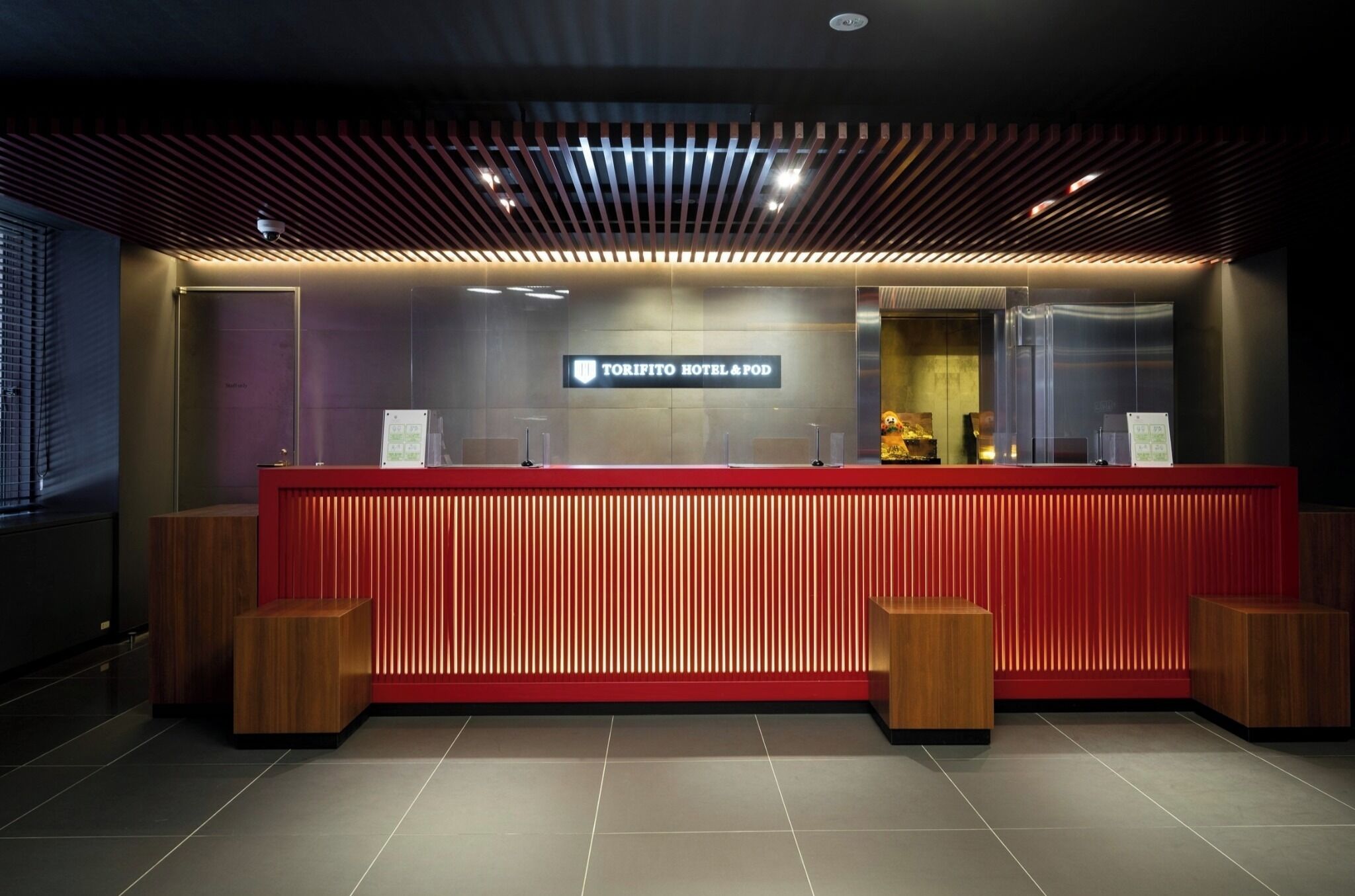 Een receptiebalie met een bordje 'TORIFITO HOTEL & POD', houten accenten en een modern plafondontwerp.