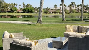 Un patio con mobiliario de mimbre y vistas a un campo de golf y una masa de agua.