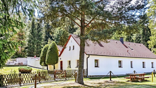 A white building with a red roof, surrounded by a wooden fence and trees.