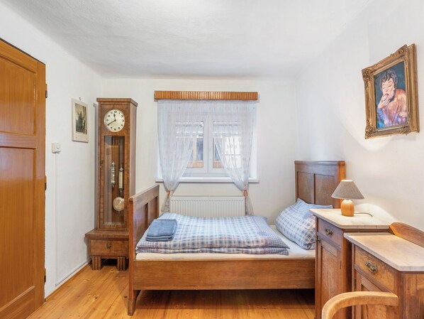 A bedroom with a wooden bed, a wooden dresser, a clock, a window with sheer curtains, and a framed picture on the wall.