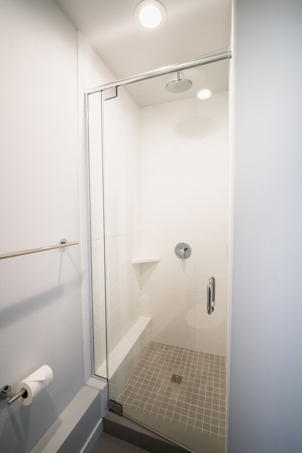 A glass-enclosed shower with a white tiled floor and a ceiling light. - Insta-worthy Views, Wine, Rooftop Firepit on Beach (Seattle)