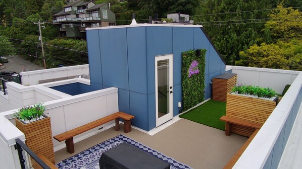 A rooftop terrace with a blue wall, a wooden bench, a small garden area, and a door.