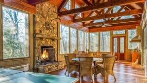 A spacious room with a stone fireplace, large windows, and a ping pong table. - Rustic Elegance. Three Fireplaces. A Crown Jewel of a Screened Porch | Sagee Woods (Highlands)