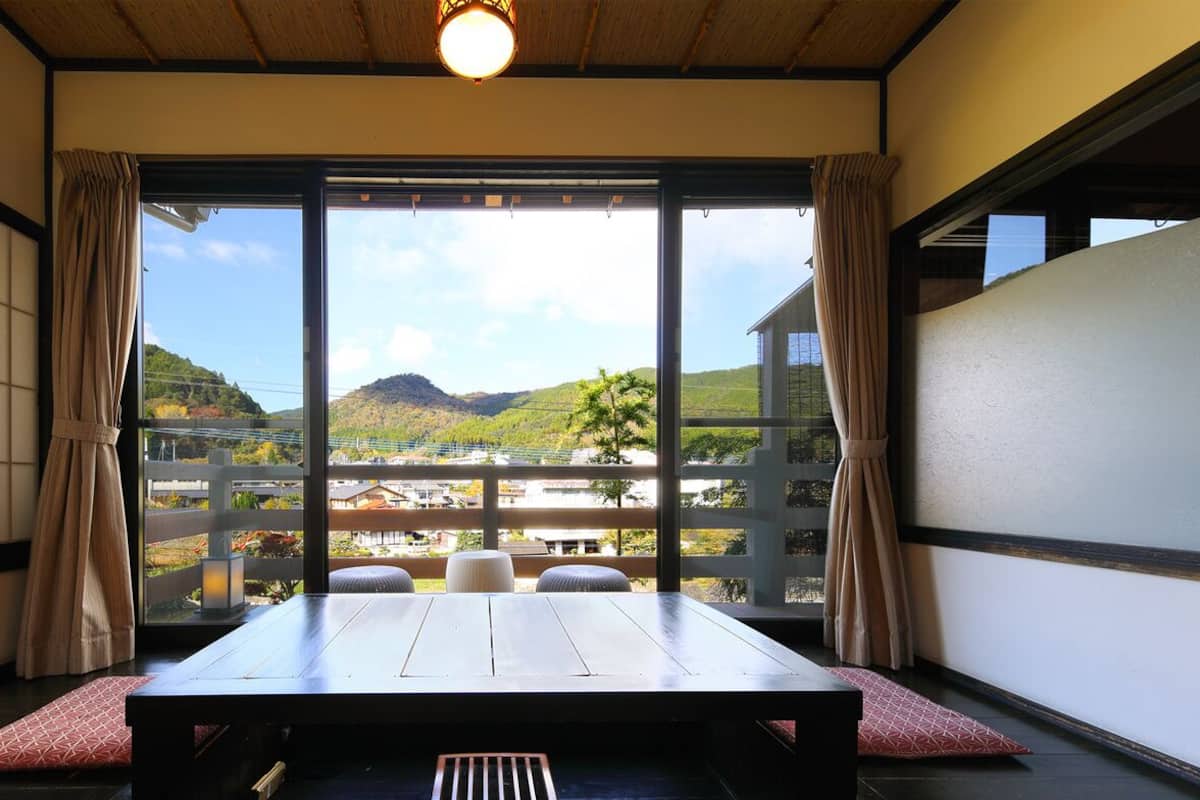 Una habitación con una mesa de madera, vistas a un paisaje montañoso y una puerta corredera con cortinas.