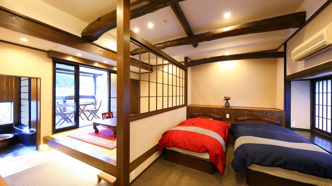 Una habitación tradicional japonesa con suelo de tatami, una cama baja de madera, puertas correderas y vistas al exterior.