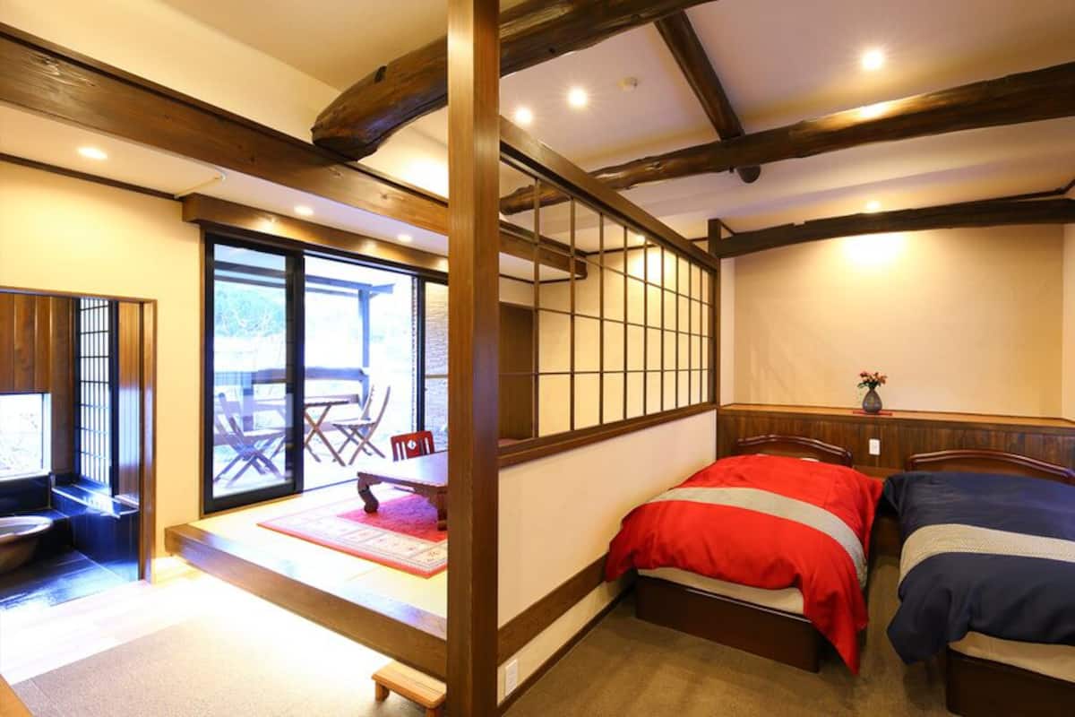 Una habitación tradicional japonesa con suelo de tatami, una cama baja de madera, puertas correderas y vistas al exterior.