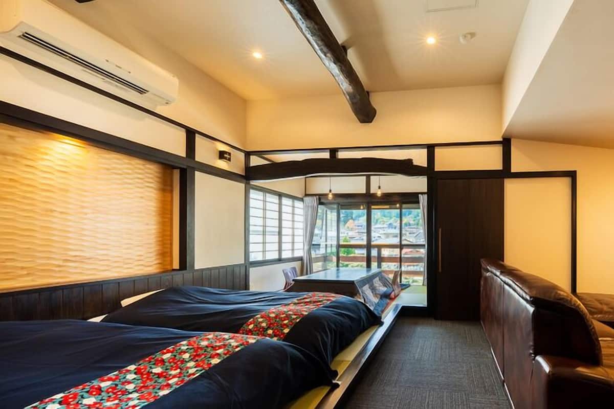 Una habitación de hotel con dos camas, un sofá, un ventanal con vistas y un techo con vigas a la vista.