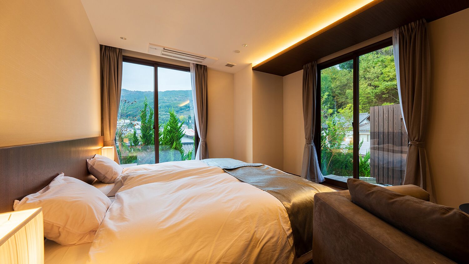 Habitación de hotel con una cama grande, un sofá, una ventana con cortinas y un equipo de aire acondicionado.