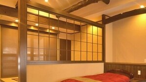 Ein traditioneller japanischer Raum mit Tatami-Boden, einem niedrigen hölzernen Bett mit roter und blauer Bettdecke und einer verschiebbaren Shoji-Schiebetür.
