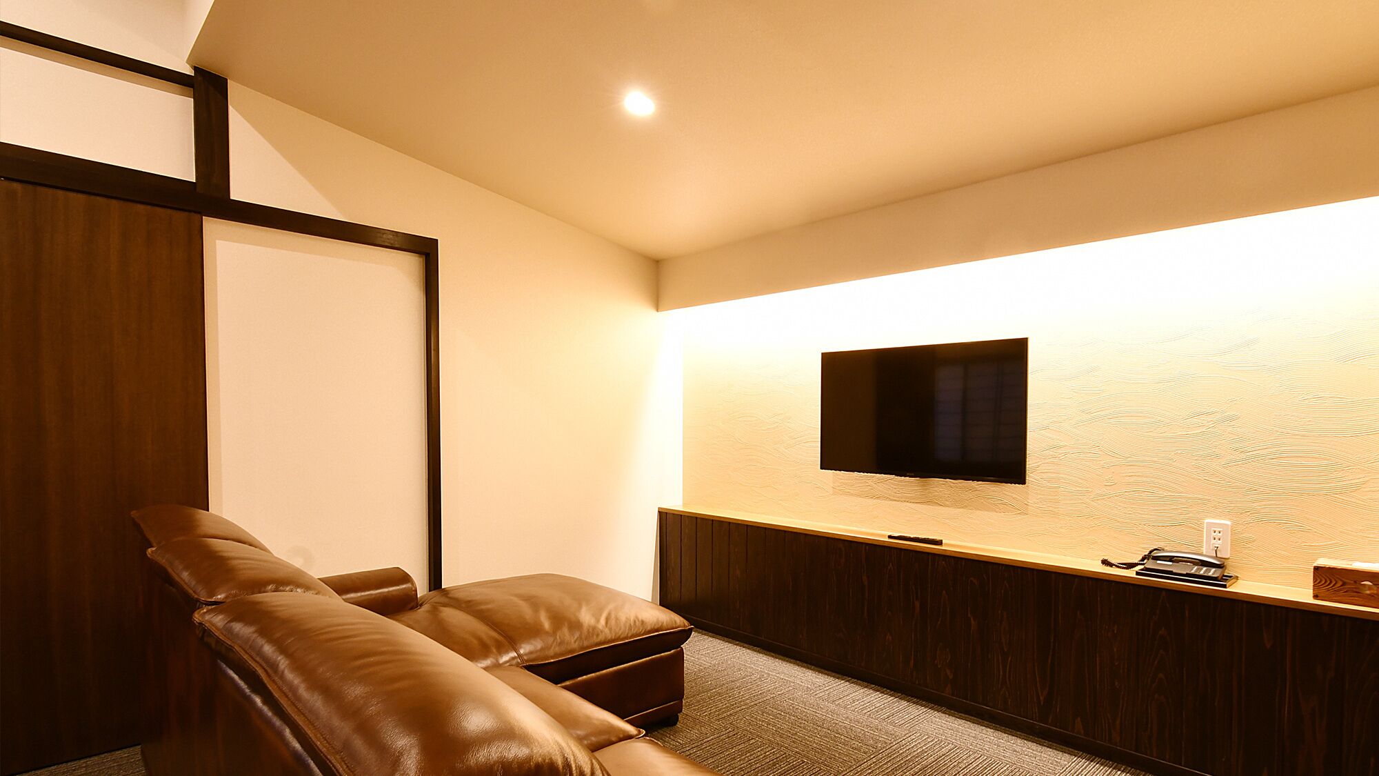 Habitación con sofá de cuero, televisor de pantalla plana montado en la pared, mueble de madera y piso alfombrado.