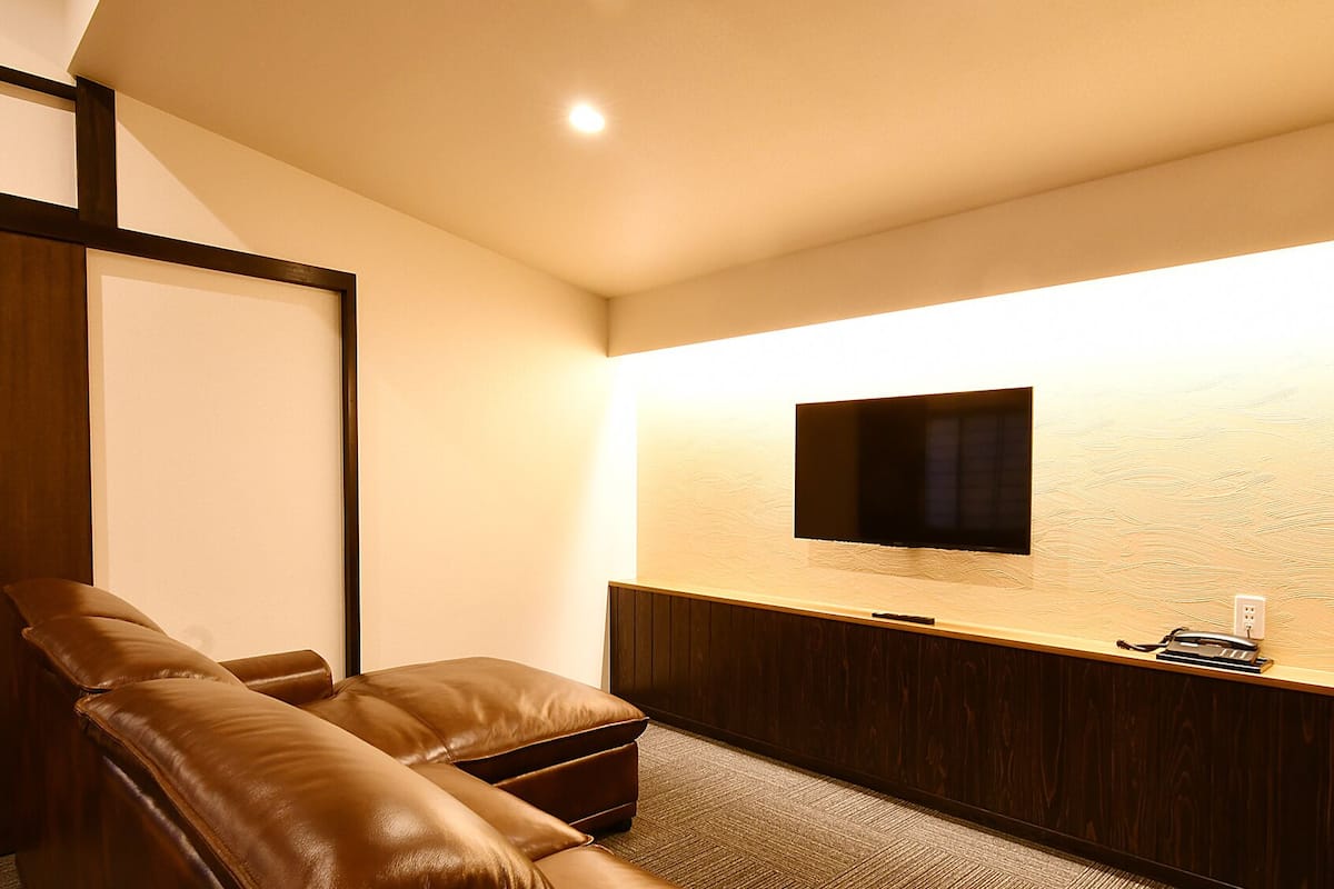 Habitación con sofá de cuero, televisor de pantalla plana montado en la pared, mueble de madera y piso alfombrado.