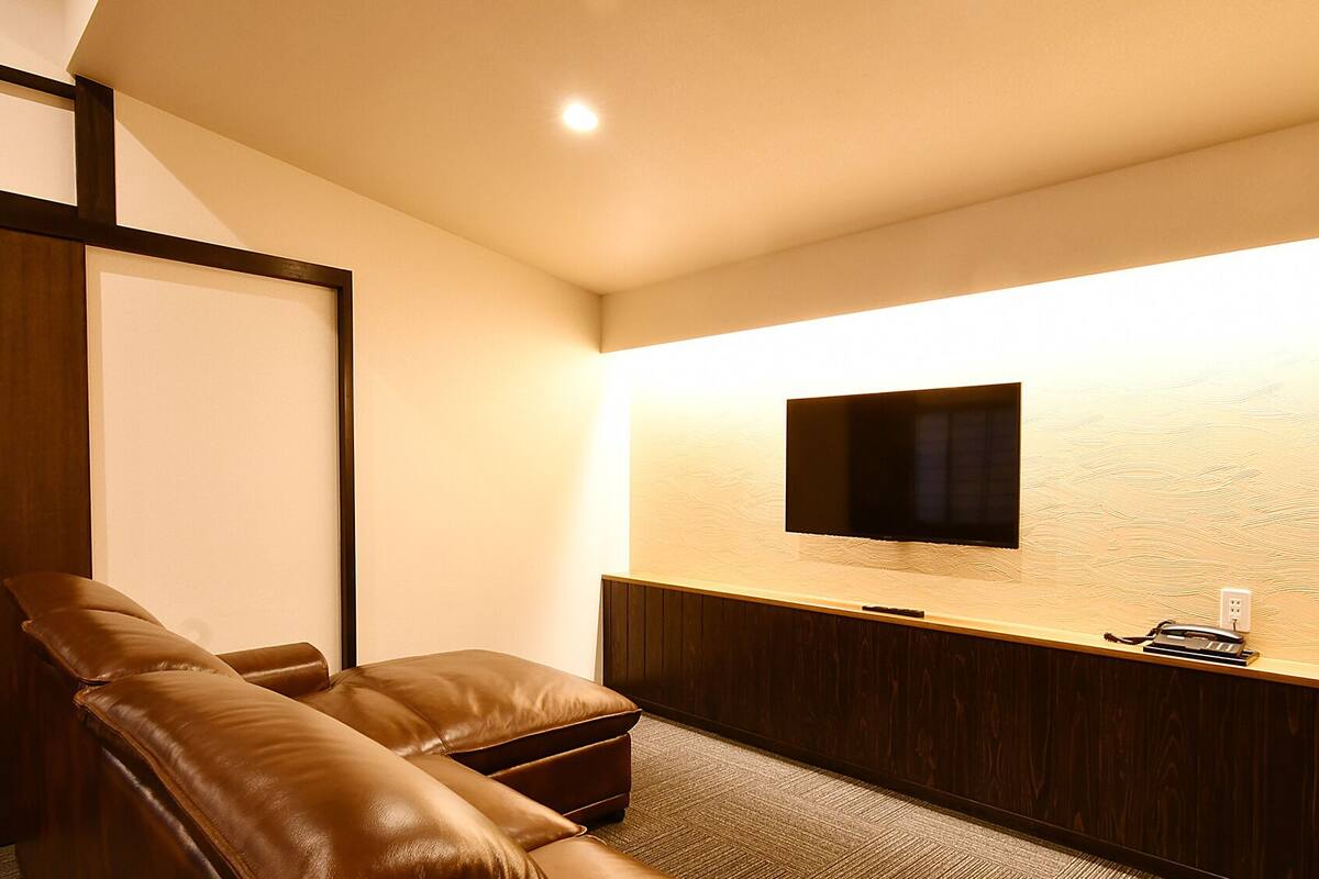 A room with a leather sofa, a flat-screen TV mounted on the wall, a wooden cabinet, and a carpeted floor.