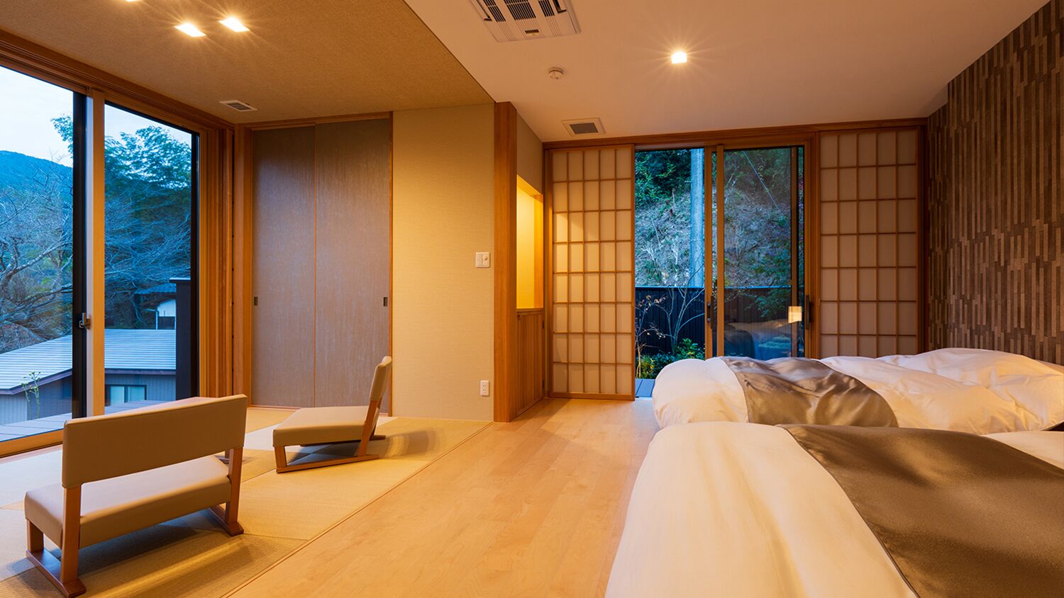 Un dormitorio moderno con una cama, un banco y puertas correderas que dan a un jardín.