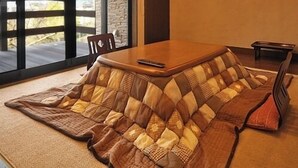 Ein Zimmer mit großem Fenster, einem Holztisch und einer Couch mit gemustertem Bezug.