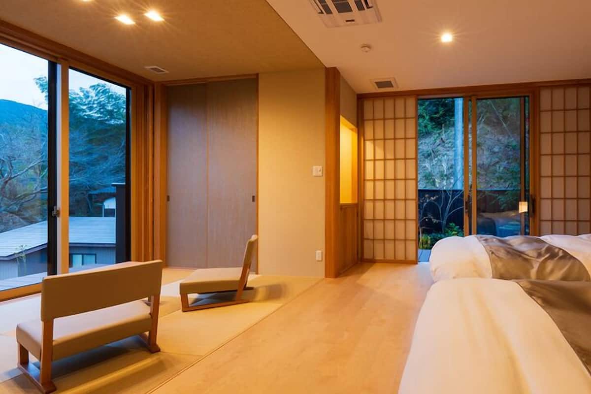 Una habitación de hotel moderna con un gran ventanal corredero, una cama, un banco y vistas al exterior.