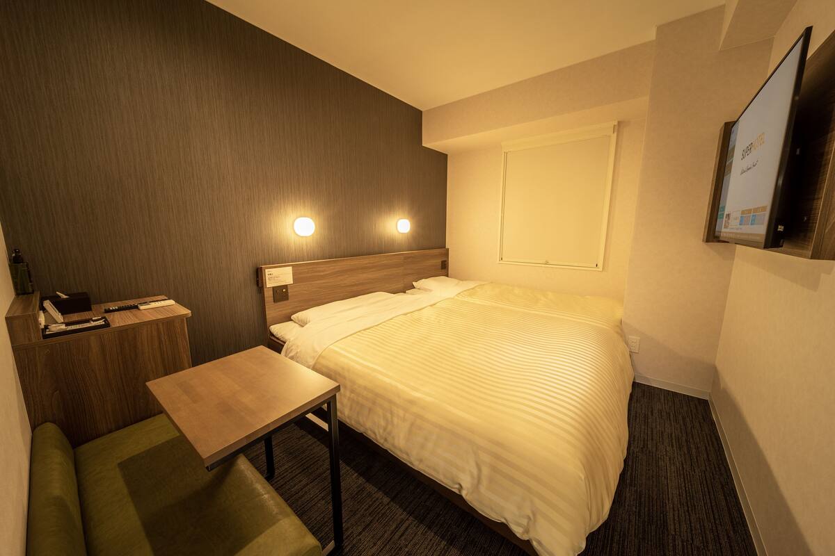 A hotel room with a bed, a desk, a chair, and a television on the wall.