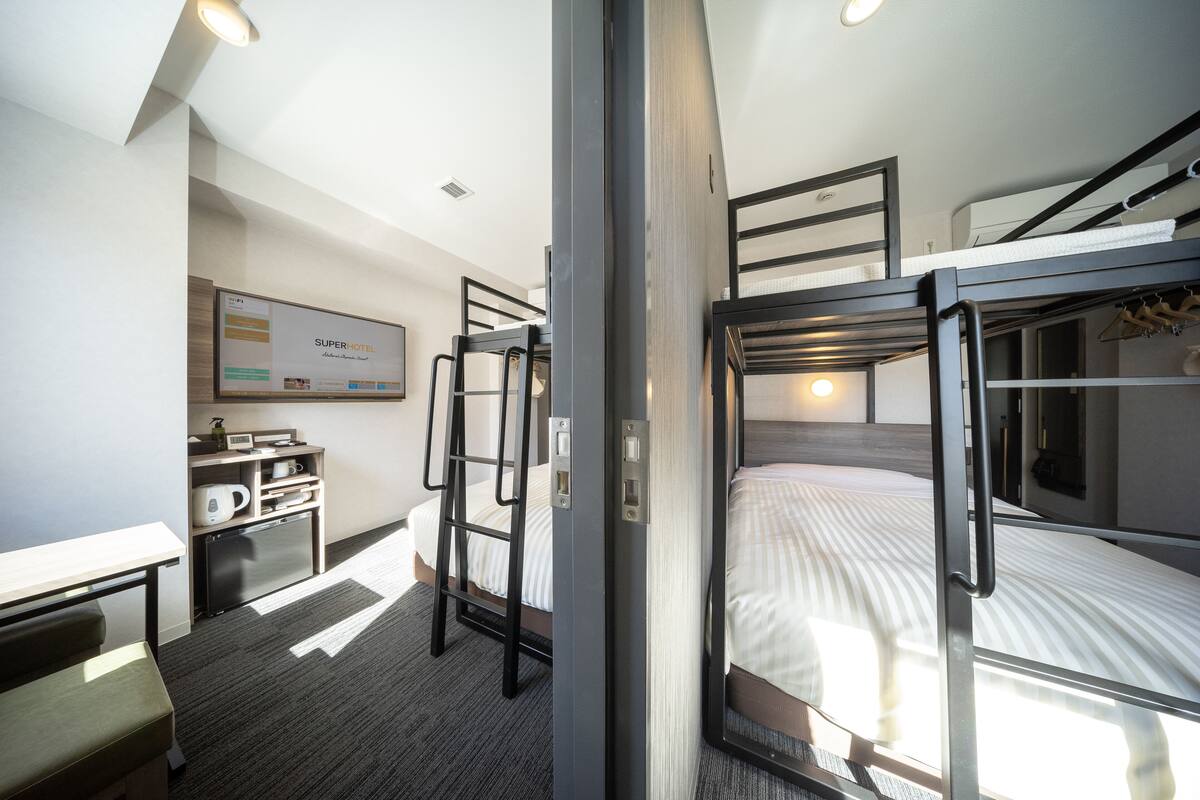 A modern hotel room with bunk beds, a desk with a coffee machine, and a small kitchenette.