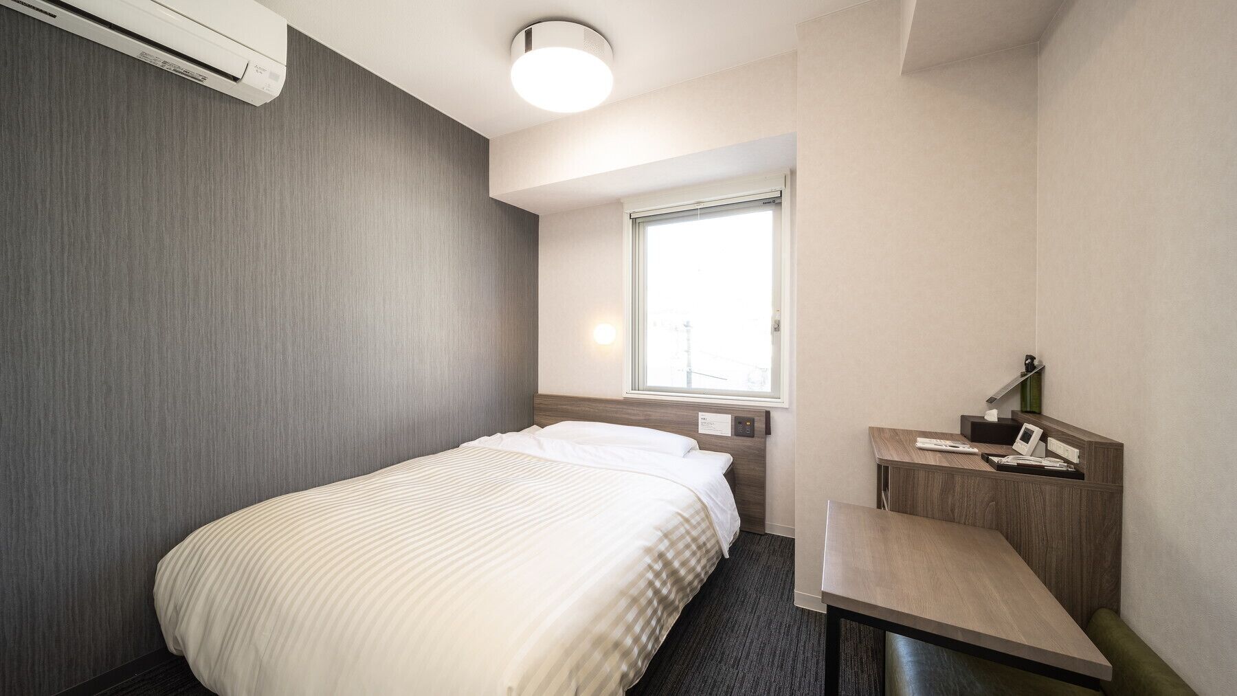 Une chambre d’hôtel équipée d’un lit, d’un bureau, d’une chaise, d’une fenêtre et d’un appareil de climatisation.