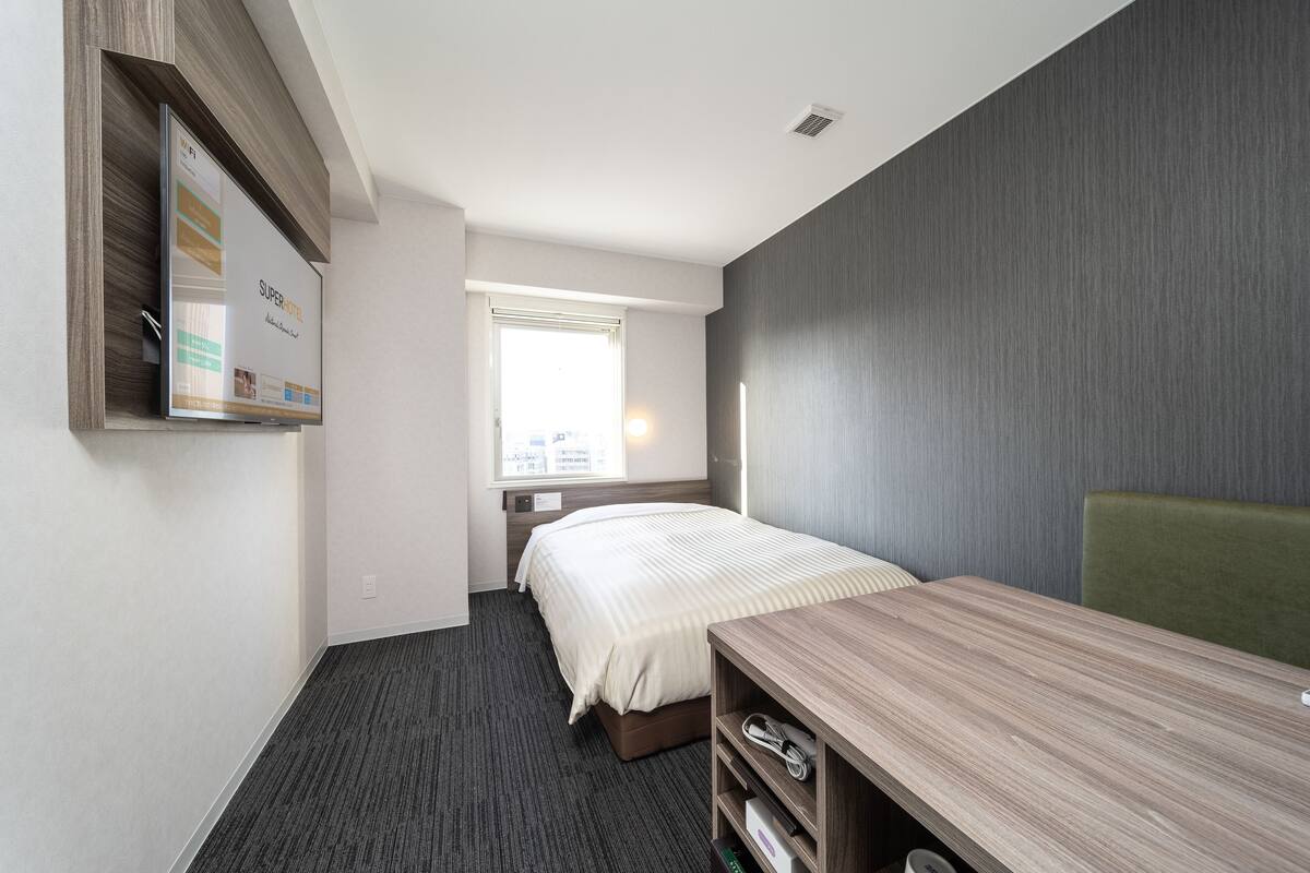 A hotel room with a bed, a desk, and a wall-mounted TV.