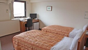 Een hotelkamer met twee bedden, een bureau met een computer en een raam met gordijnen.