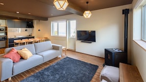 A modern living room with a sofa, a TV, a fireplace, and a kitchen area in the background. - Iroha Nozawa (Nozawaonsen)