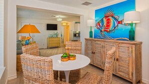 A dining area with wicker chairs, a white table, and a colorful fish painting on the wall. - Bikini Bottom 2Bed 2Bath Ocean View Huge Outdoor Pool - DOWNSTAIRS UNIT (Port Aransas)