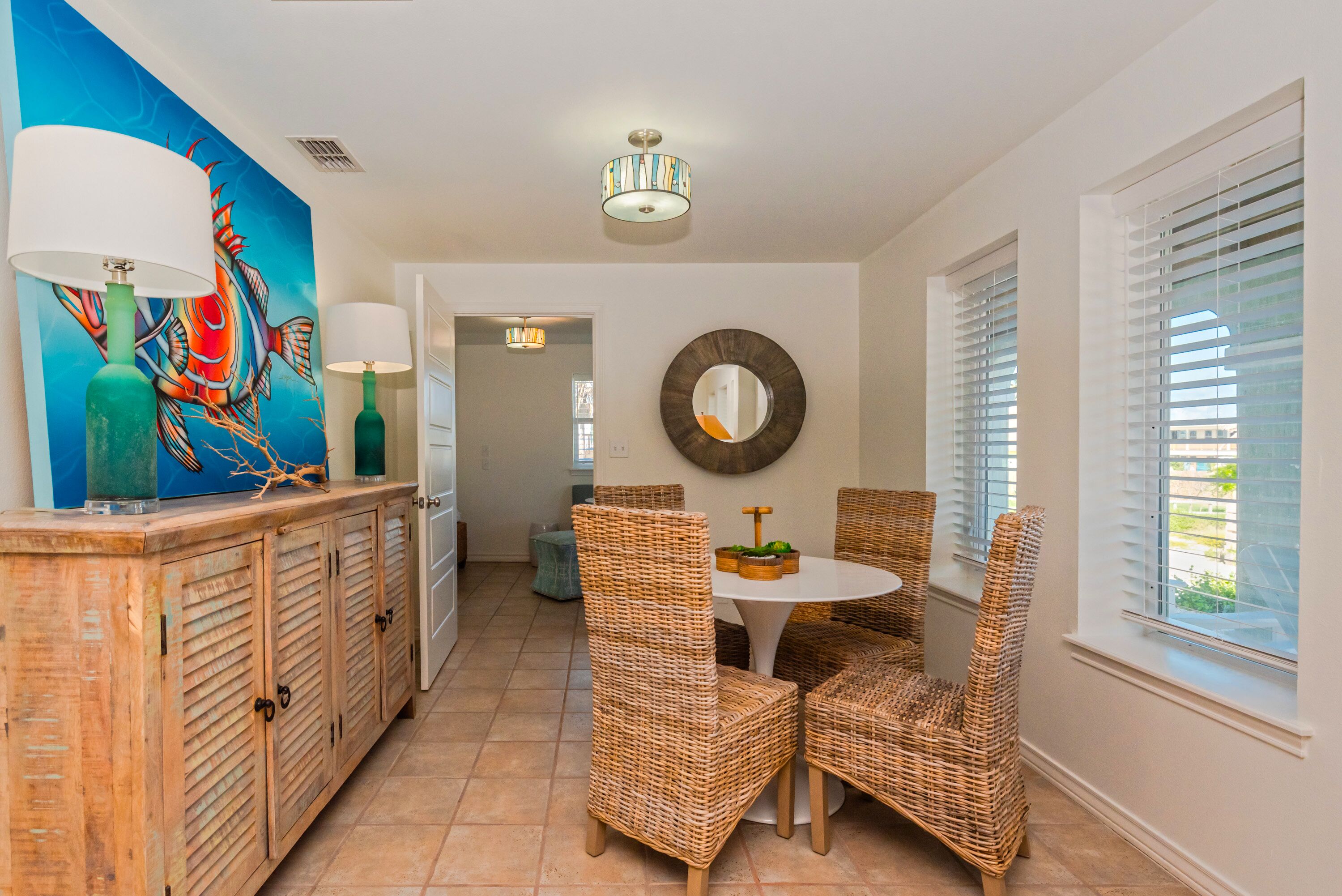 A dining area with wicker chairs, a round table, and a painting on the wall.