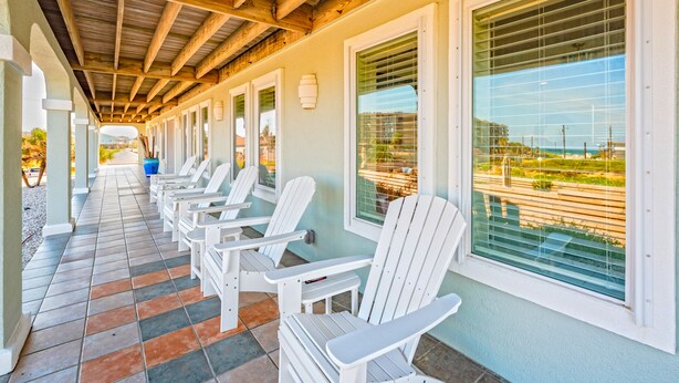 A covered outdoor seating area with white chairs and a tiled floor. - Bikini Bottom 2Bed 2Bath Ocean View Huge Outdoor Pool - DOWNSTAIRS UNIT (Port Aransas)