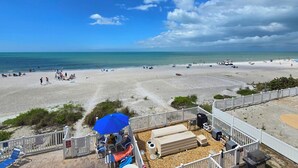 Blick auf einen Strand mit einer Terrasse, Liegestühlen und einem Grill.