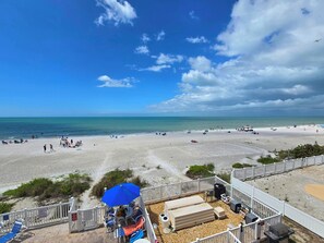 A beach view with a patio area, lounge chairs, and a barbecue grill.