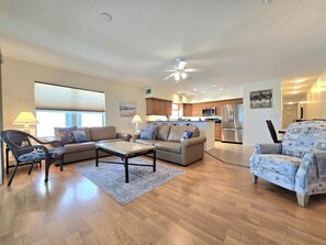 A spacious living room with a sofa, armchair, and coffee table, a kitchen with modern appliances, and a dining area with a patterned chair. - Ocean Side 306 Corner Unit Beach front (Indian Rocks Beach)