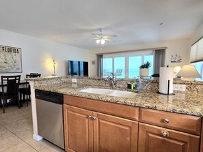 A kitchen with granite countertops, wooden cabinets, a dishwasher, and a ceiling fan.