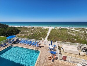 A pool area with lounge chairs and umbrellas, a beach view, and a pathway leading to the beach.
