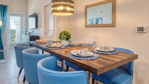 A dining area with a wooden table set for four, blue chairs, a hanging light fixture, a framed artwork, and a thermostat on the wall. - VCR4-403 - 3BR Condo near Universal and Disney (Orlando)