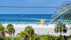 Een strand met palmbomen, een badwachterstoeltje en parasols.