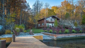 Un chalet au bord du lac, doté d’une terrasse en bois, d’un foyer extérieur et offrant une vue sur la forêt environnante.