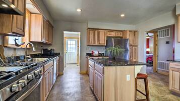 A spacious kitchen with wooden cabinets, a central island, stainless steel appliances, and a view into the living area.