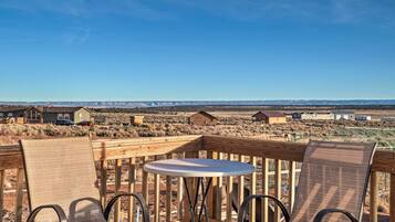 A wooden deck with two chairs and a table, overlooking a desert landscape with houses in the distance.