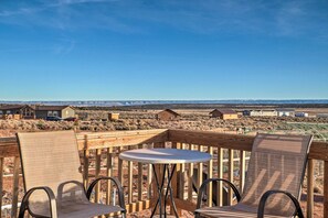 Eine Holzterrasse mit zwei Stühlen und einem Tisch, mit Blick auf eine Wüstenlandschaft mit Häusern in der Ferne.