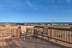Eine Holzterrasse mit zwei Stühlen und einem Tisch, mit Blick auf eine Wüstenlandschaft und entfernte Gebäude.