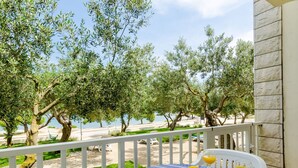 A balcony with a table set for breakfast, overlooking a beach with olive trees and a clear sky. - Apartments Glavor (Janjina)