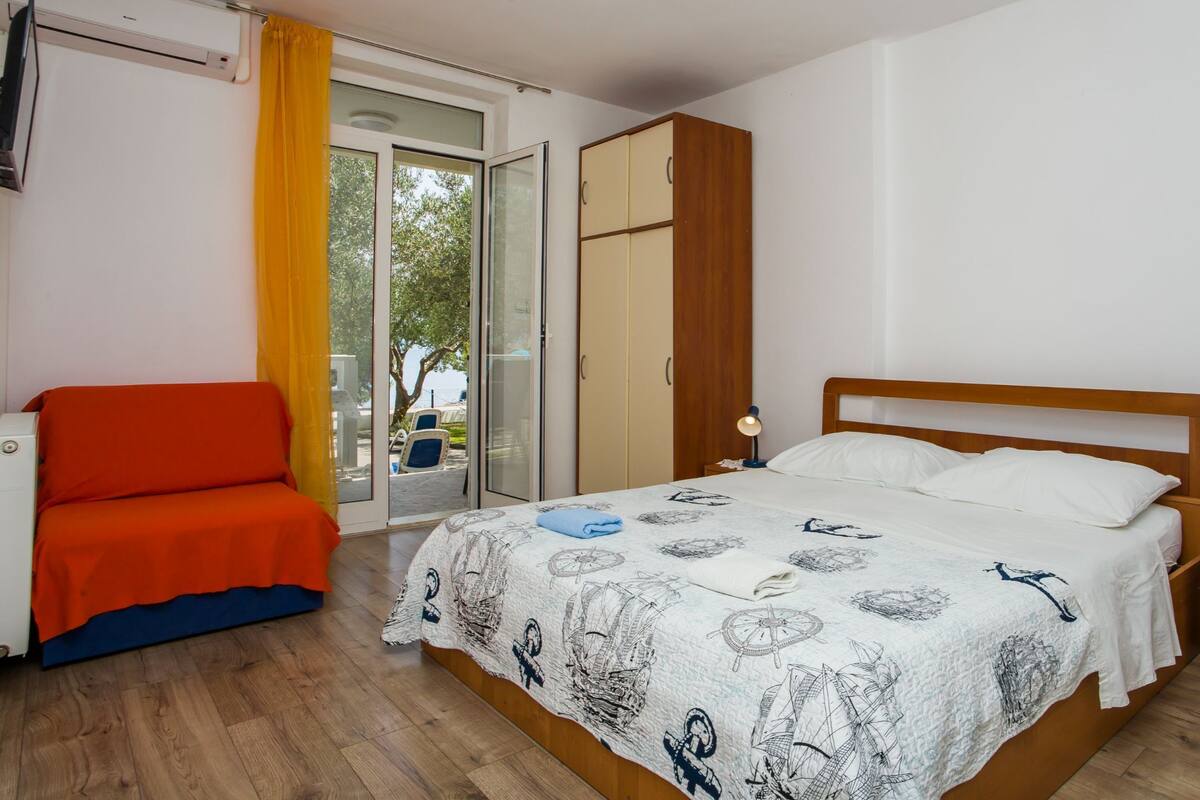 Un dormitorio con cama, una silla, armario y ventana con cortinas.