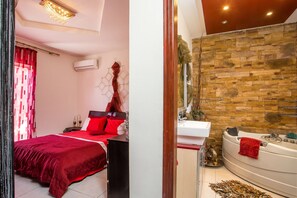 A bedroom with a large bed, a red blanket, and a red pillow. There is a bathroom with a stone wall, a bathtub, and a sink. - Villa Marilia - Lux home near Beach (Rhodes)