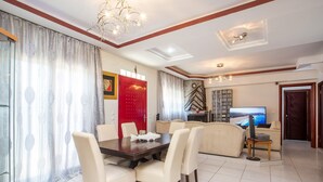 A dining area with a dark wooden table and white chairs, a red door, and a television in the background. - Villa Marilia - Lux home near Beach (Rhodes)