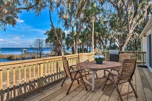 Une terrasse en bois avec une table et des chaises, donnant sur une étendue d’eau et des arbres.