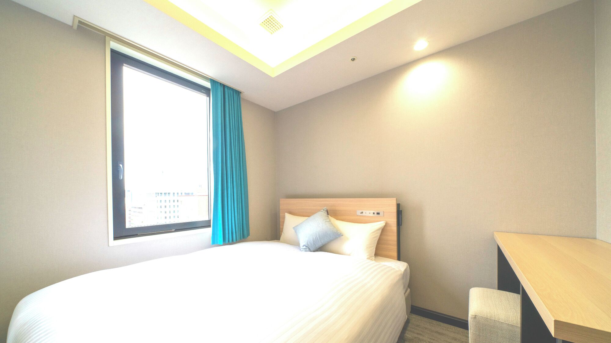 Une chambre d’hôtel avec un lit, un bureau, une fenêtre avec des rideaux et un luminaire au plafond.