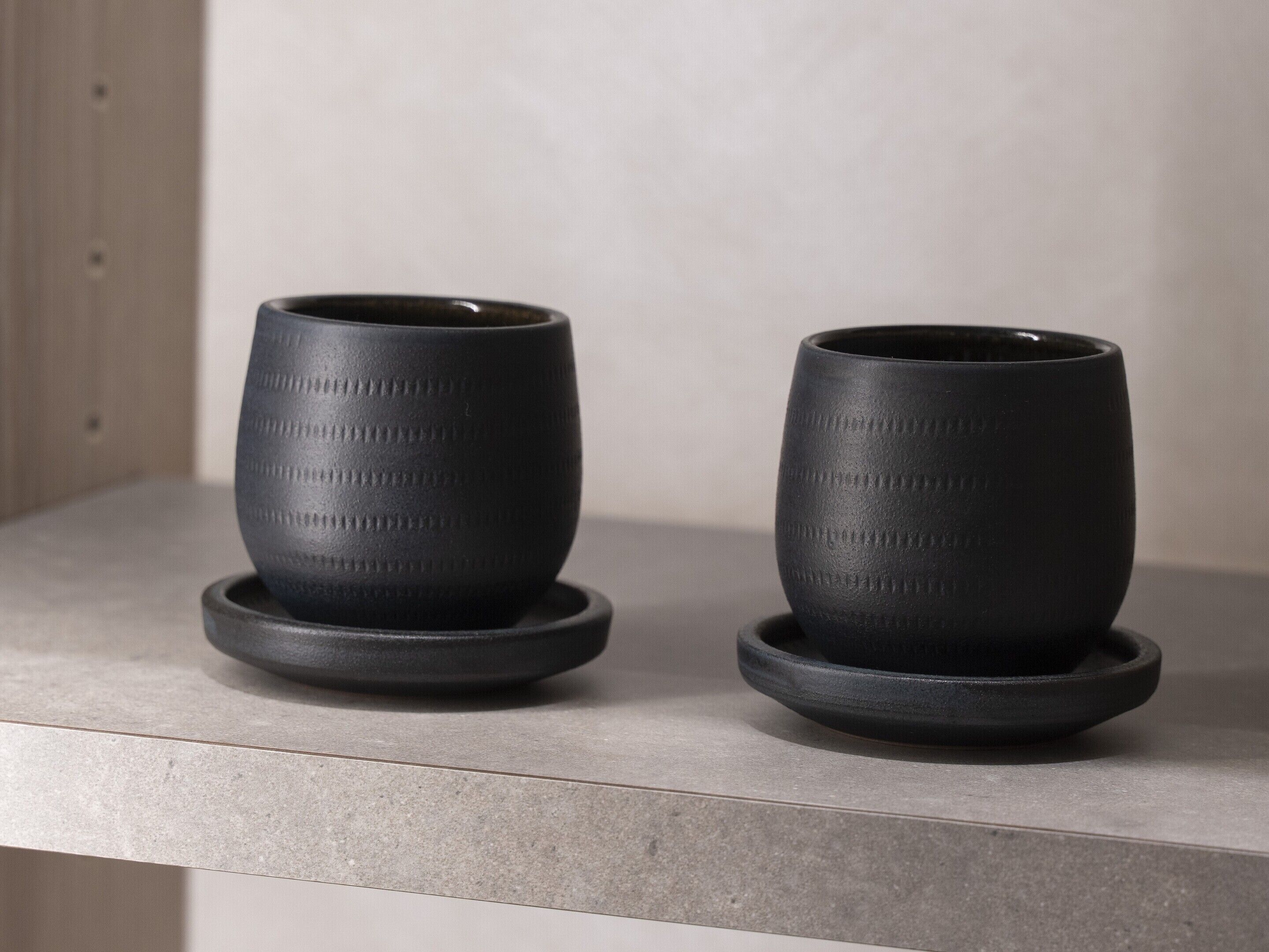 Dos tazas de cerámica negra con diseños en relieve sobre una superficie de color claro.
