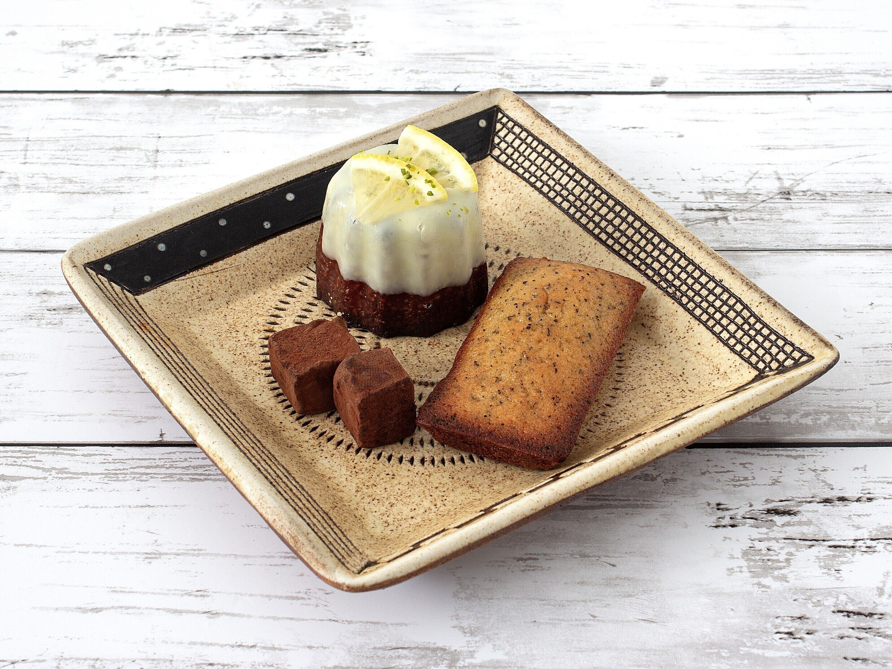Une assiette carrée en céramique, sur laquelle sont disposés un dessert et deux morceaux de pain, est posée sur une table en bois rustique.