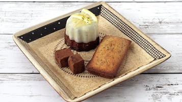 Une assiette carrée en céramique, sur laquelle sont disposés un dessert et deux morceaux de pain, est posée sur une table en bois rustique.