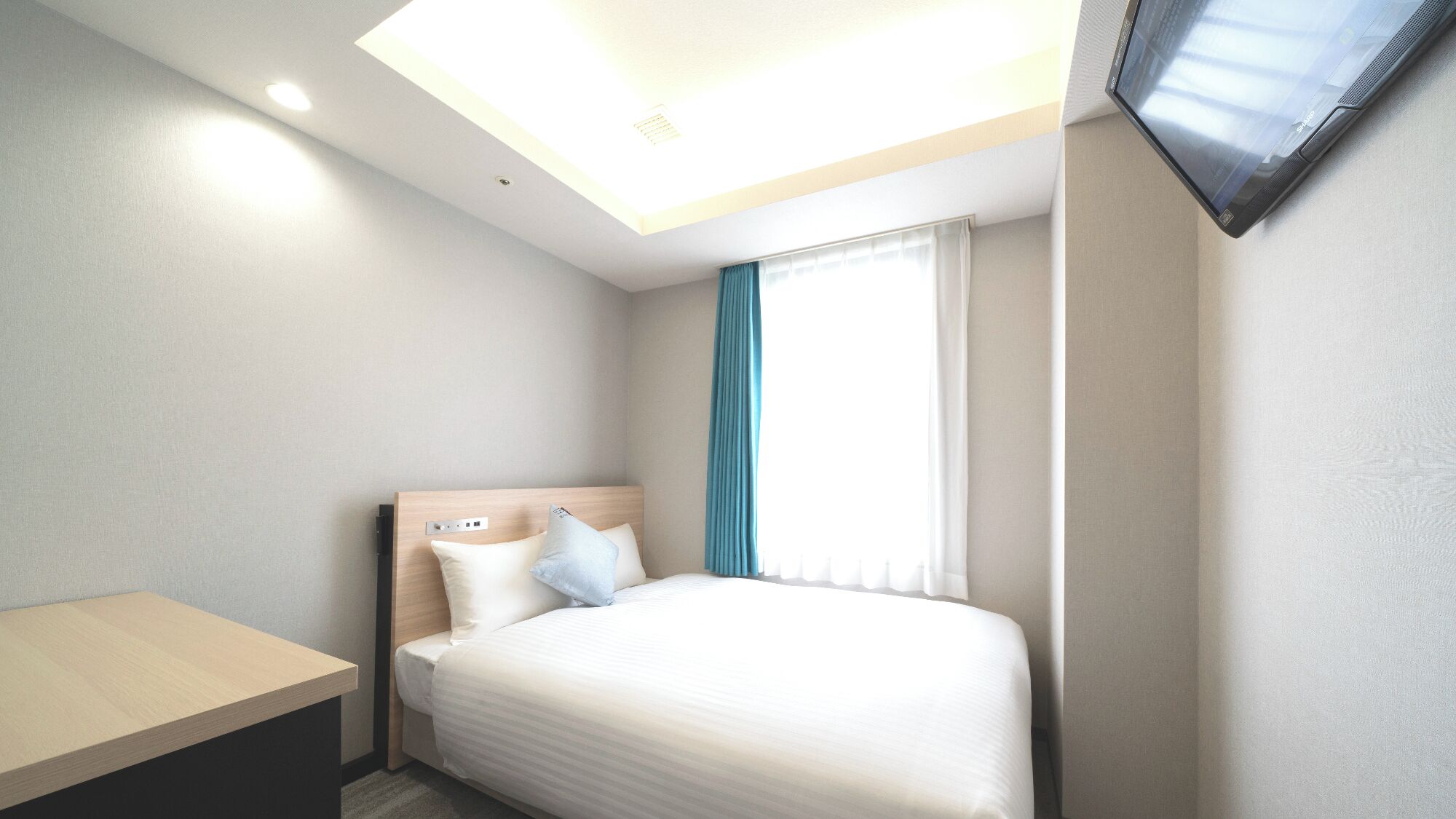 Une chambre d’hôtel avec un lit, un bureau, un téléviseur fixé au mur et une fenêtre avec des rideaux.